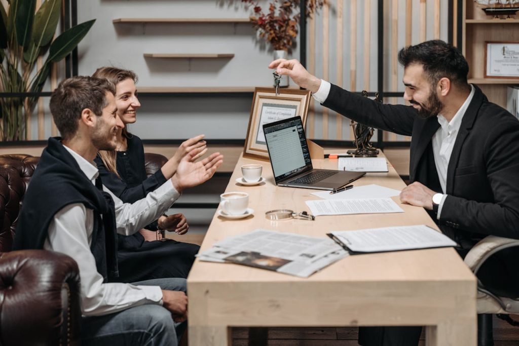 Business professional handing keys to smiling clients at an office desk during a consultation.
